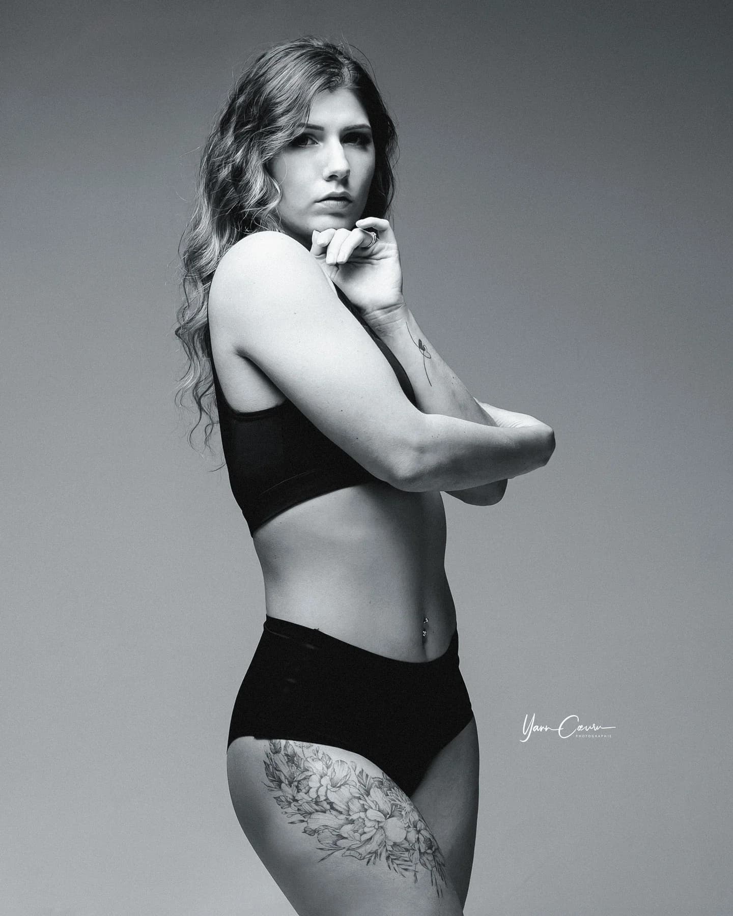 Photographe boudoir en Ardèche — femme tatouée en lingerie noire, pose de profil sensuelle en studio, clair-obscur noir et blanc